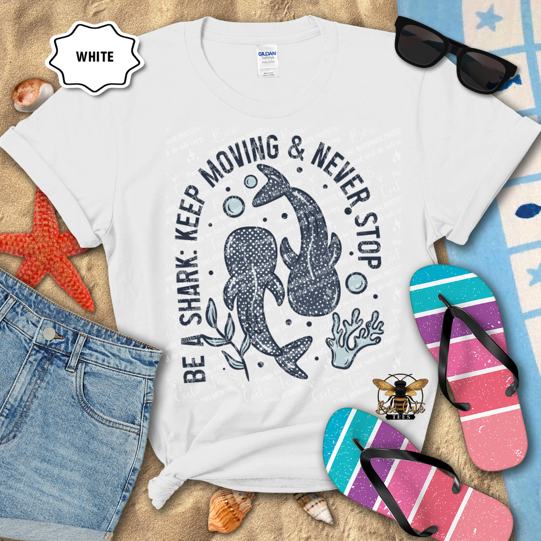 White t-shirt with shark graphic and text on a beach-themed background with sunglasses, flip-flops, and denim shorts.