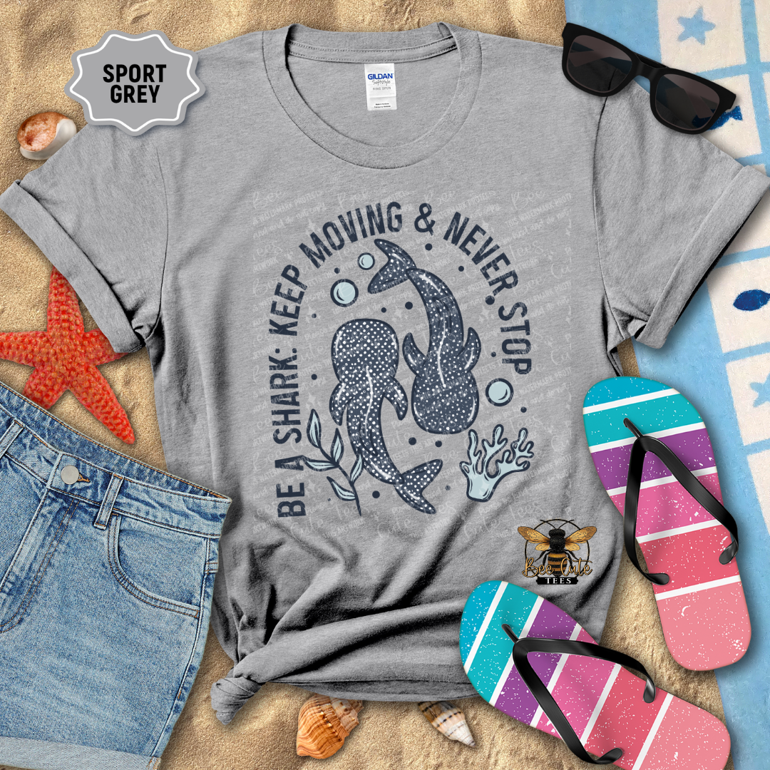 Gray t-shirt with shark graphic and text, sunglasses, flip-flops, and jeans on a beach-themed background