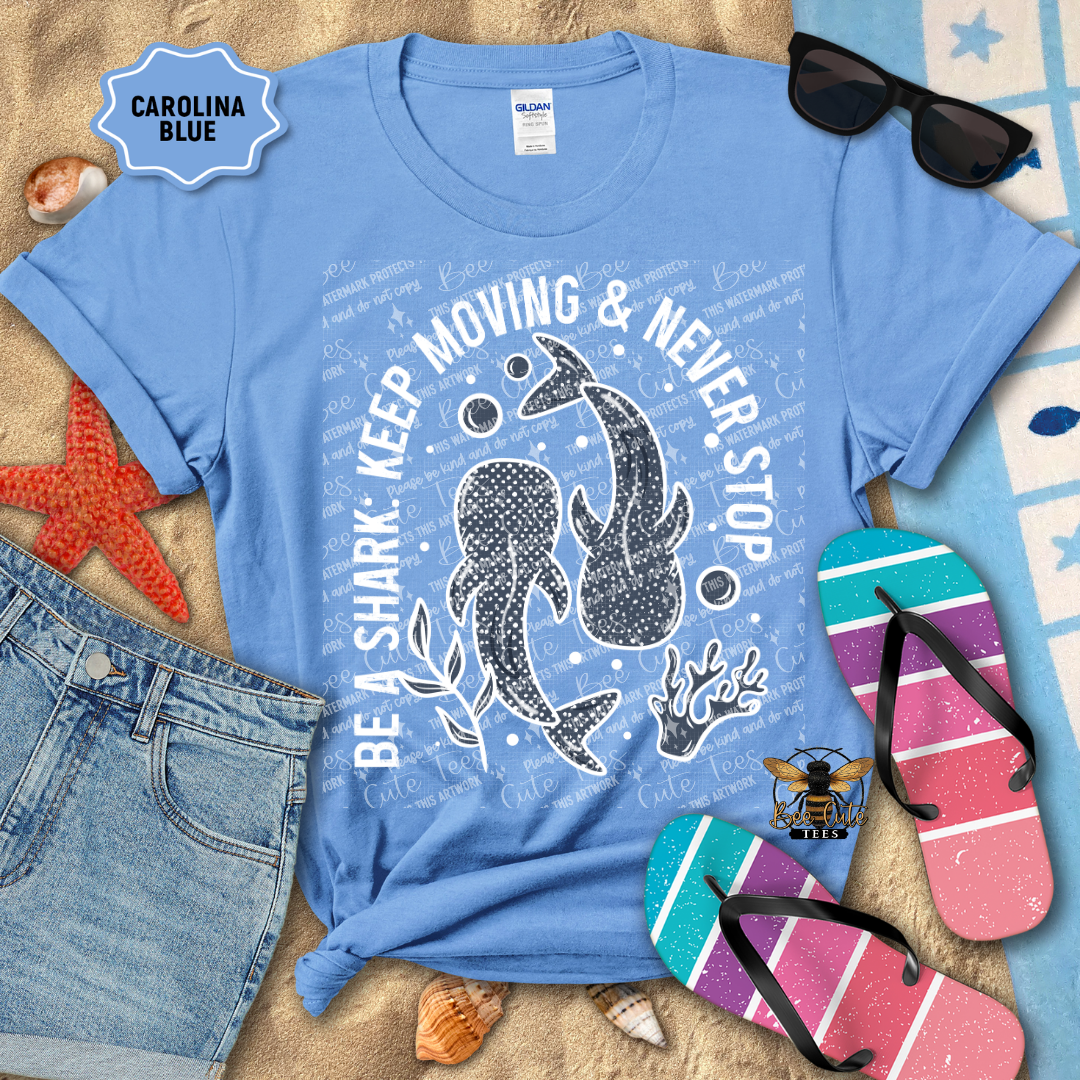 Blue t-shirt with shark design and text, sunglasses, flip-flops, and beach items on a sandy background