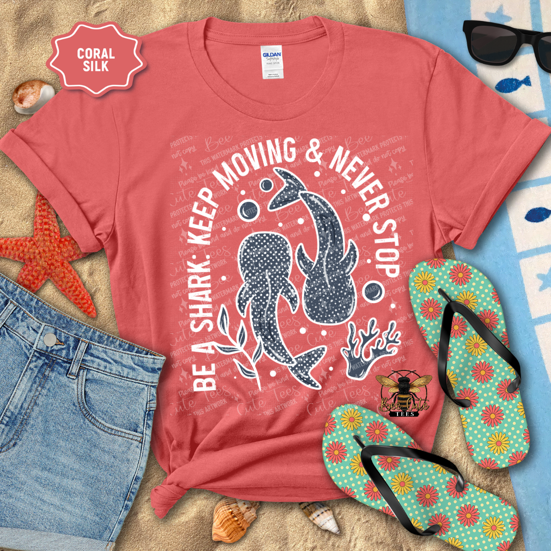 Coral t-shirt with shark graphic and text on a beach-themed background