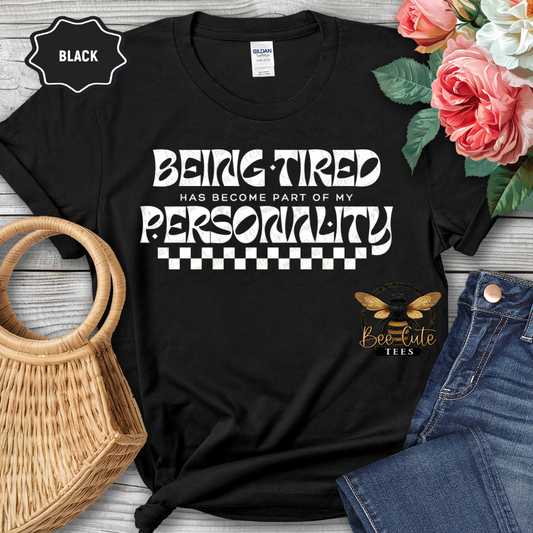 Black t-shirt with humorous text design on a wooden surface with flowers and jeans.