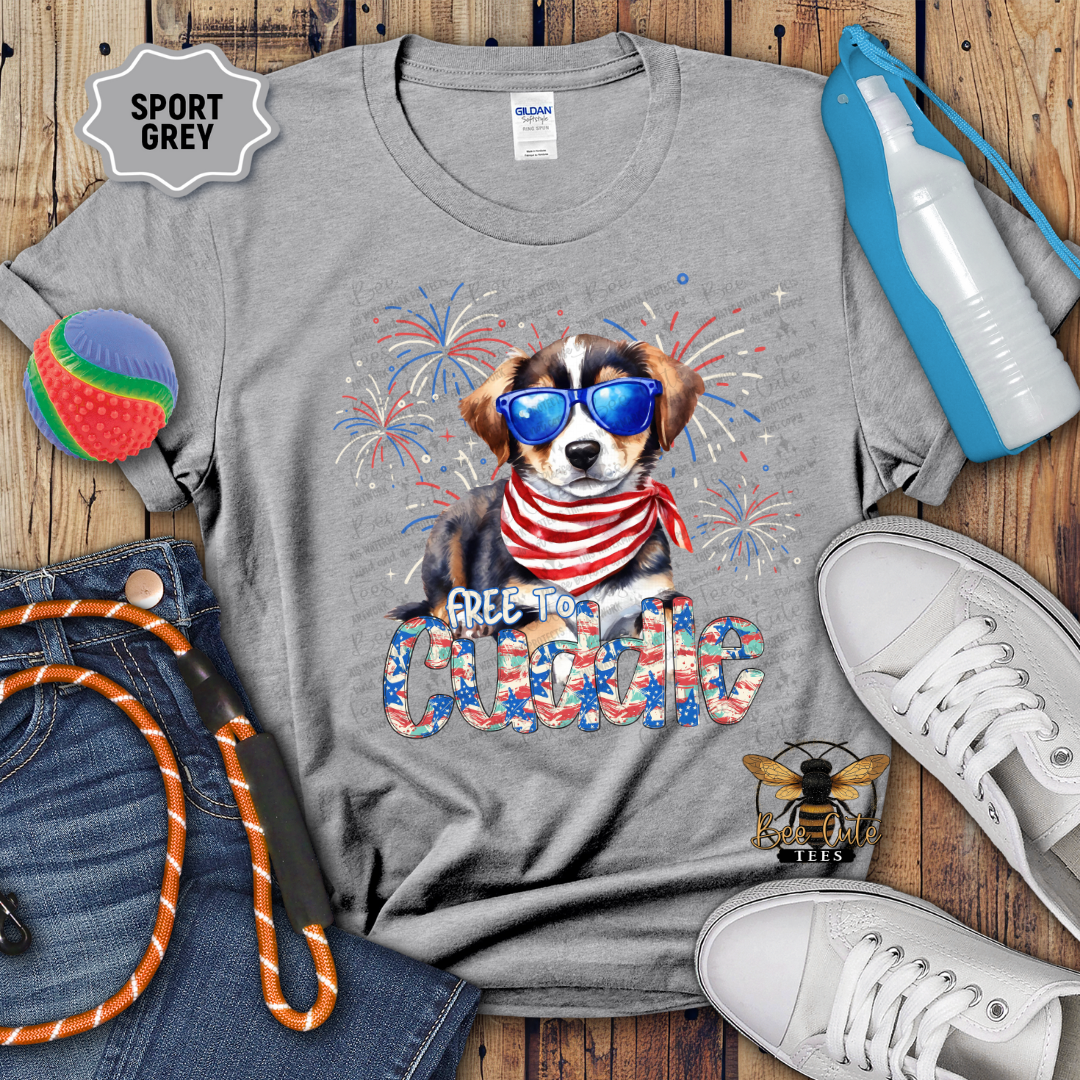 Gray t-shirt with a dog graphic and 'Free too Cuddle' text, surrounded by accessories on a wooden surface.