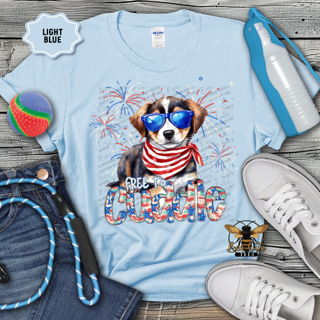 Light blue t-shirt with a dog graphic and 'Free to cuddle' text, surrounded by accessories on a wooden surface.