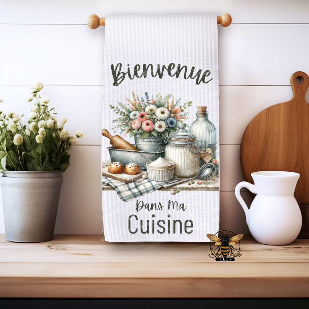 Kitchen towel with floral design and text on a wooden shelf with decor items.