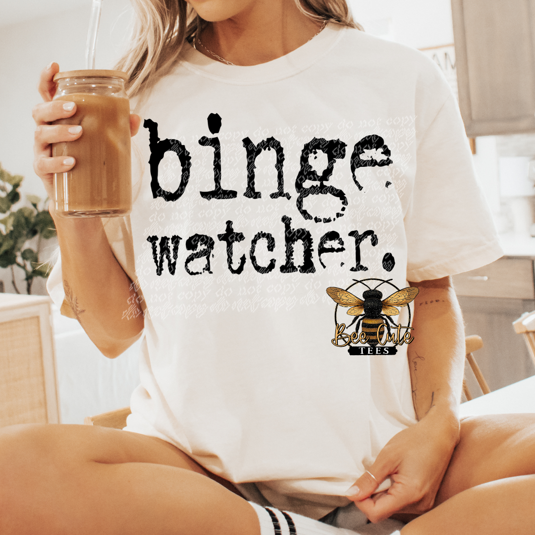 Person wearing a white t-shirt with 'binge watcher' text and holding a drink.