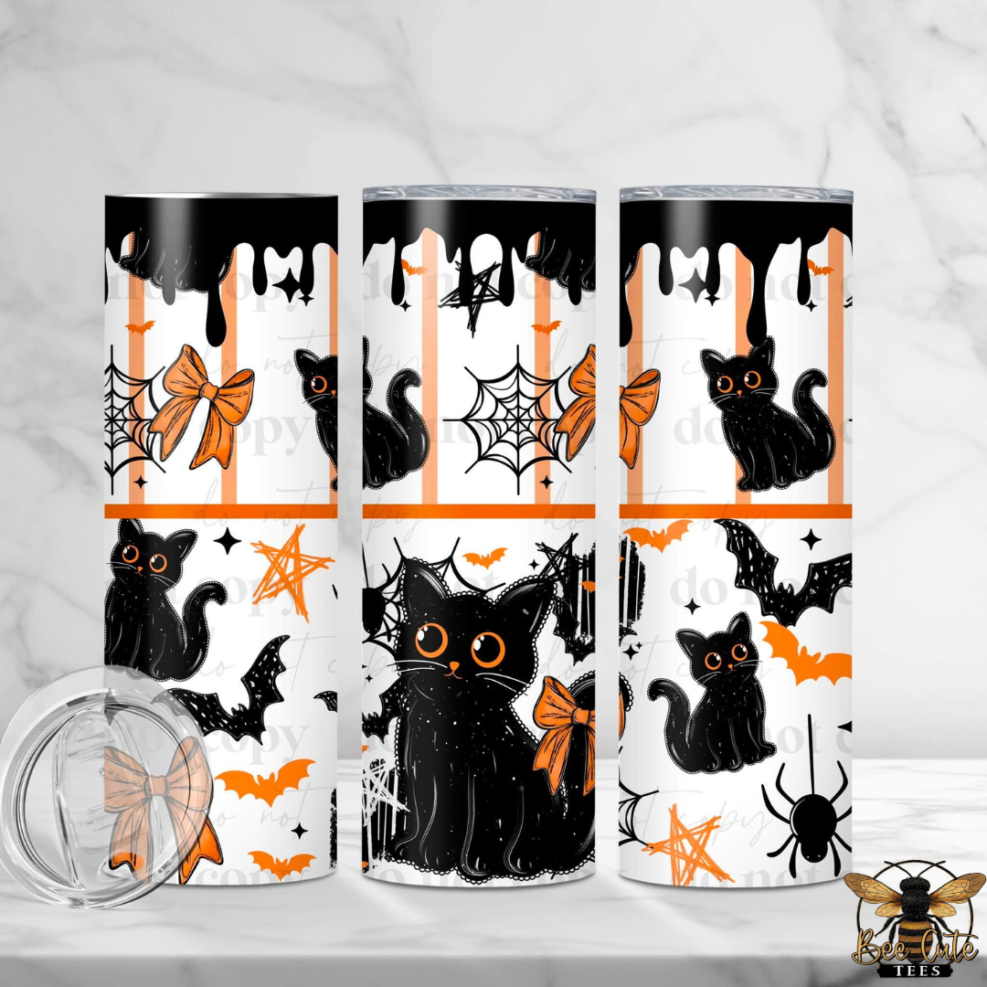 Three tall skinny tumblers with a Halloween-themed print featuring black cats, orange bows, bats, spiders, and stars on a white background with orange stripes. A clear lid is shown in the foreground on a white marble surface.