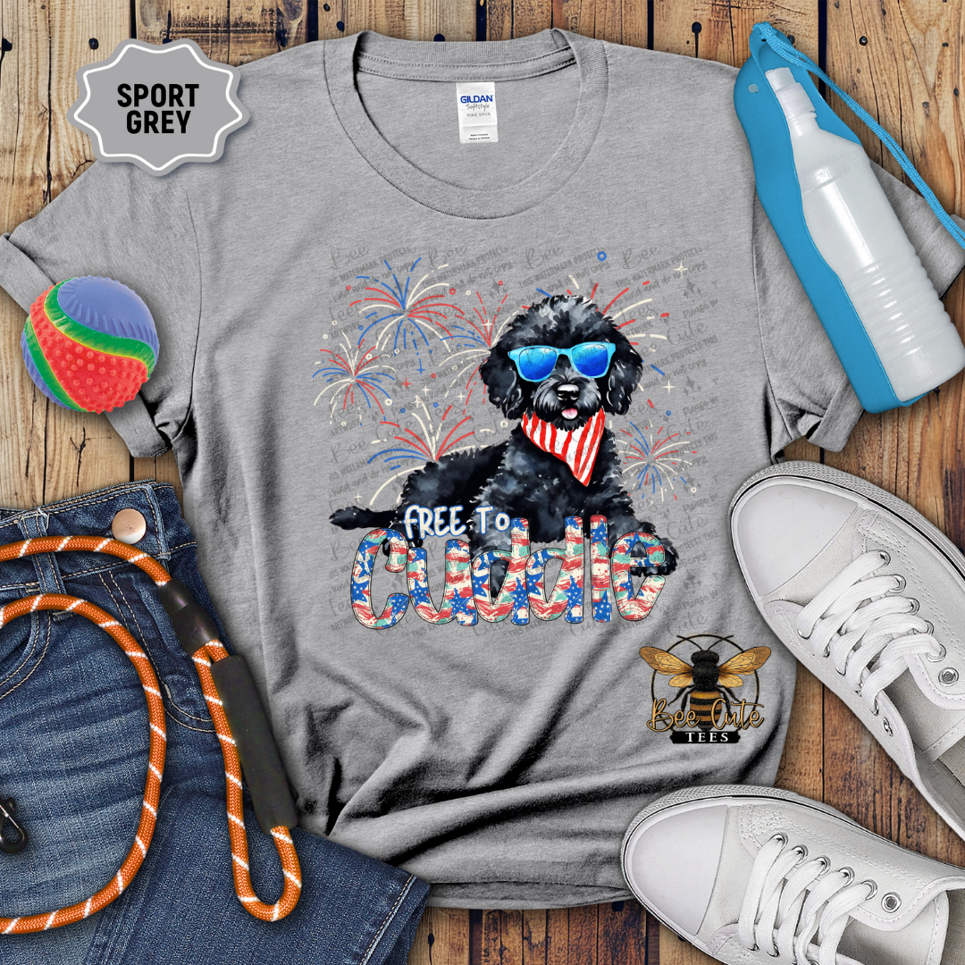 Gray t-shirt with a dog graphic and text, surrounded by jeans, shoes, and accessories on a wooden surface.