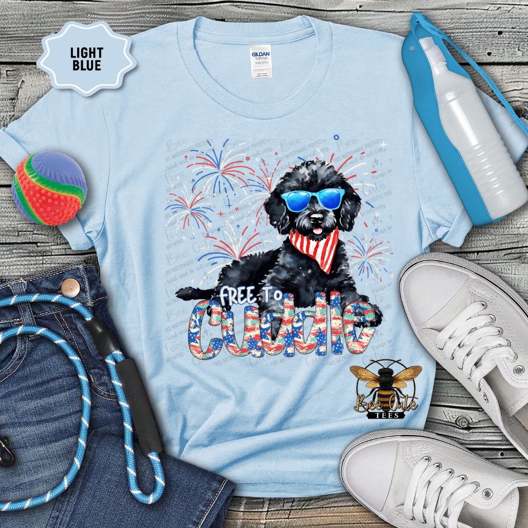 Light blue t-shirt with a black dog graphic and text, surrounded by casual items on a wooden surface.