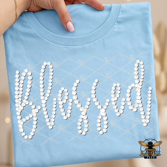 Light blue t-shirt with 'Blessed' text made of faux white pearls, held by a hand.