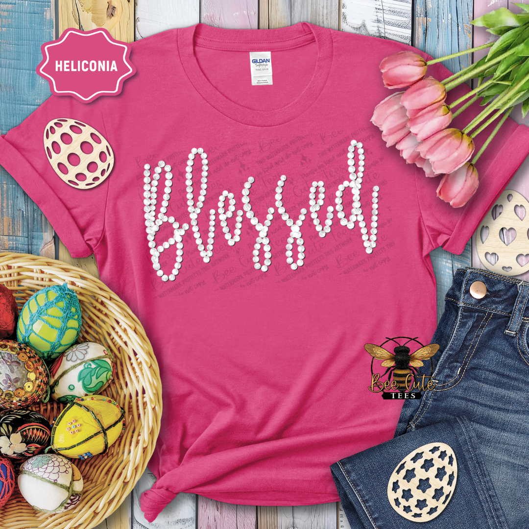 Pink t-shirt with 'Blessed' text, surrounded by Easter decorations on a wooden surface.