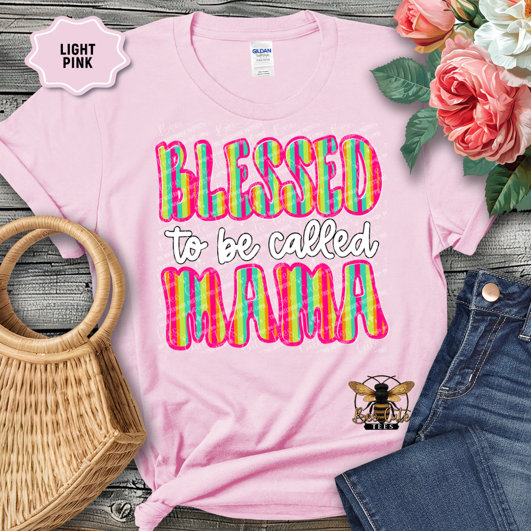 Light pink t-shirt with 'Blessed to be called MAMA' text, surrounded by flowers and denim jeans on a wooden surface.