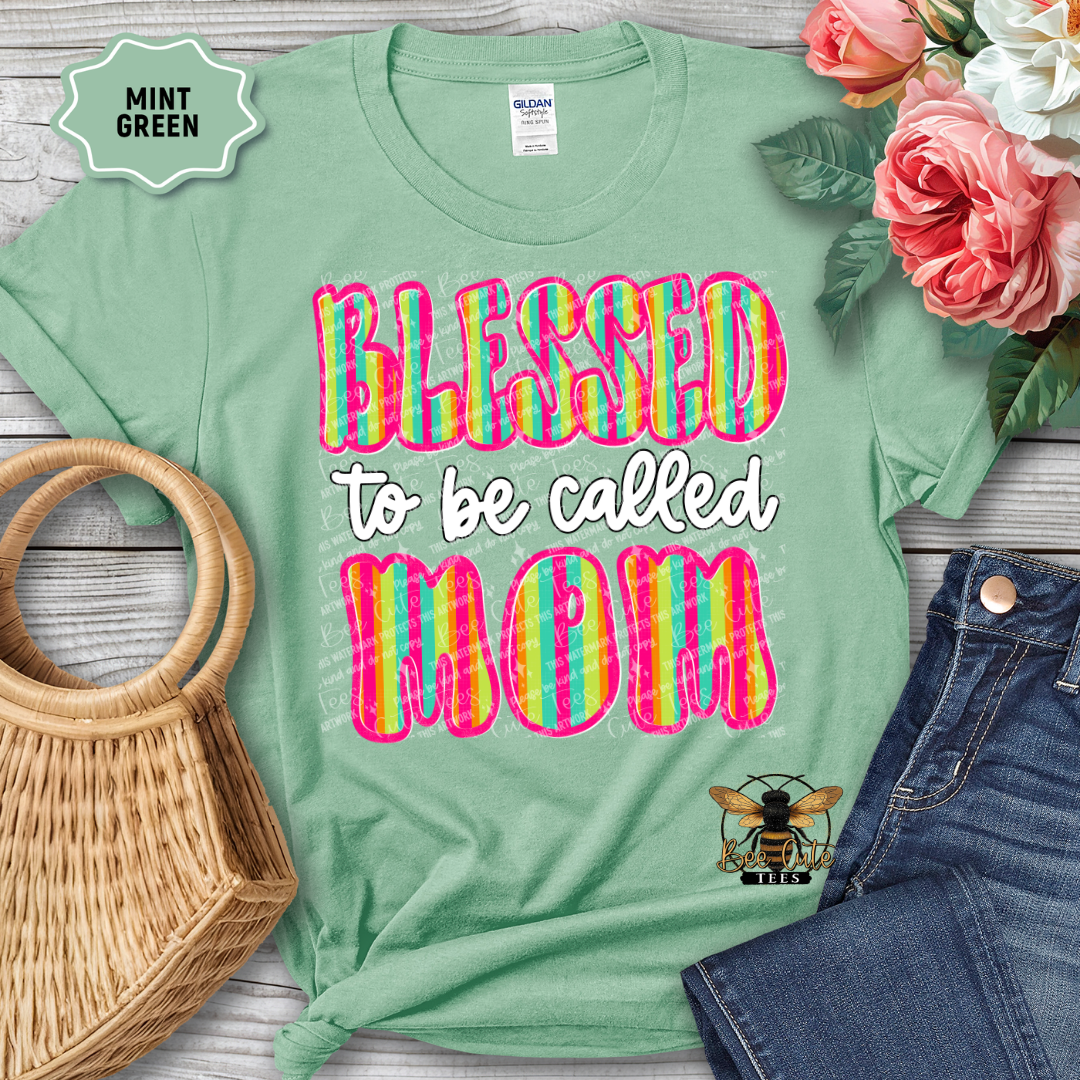 Mint green t-shirt with 'Blessed to be called Mom' text, surrounded by flowers and denim jeans on a wooden surface.