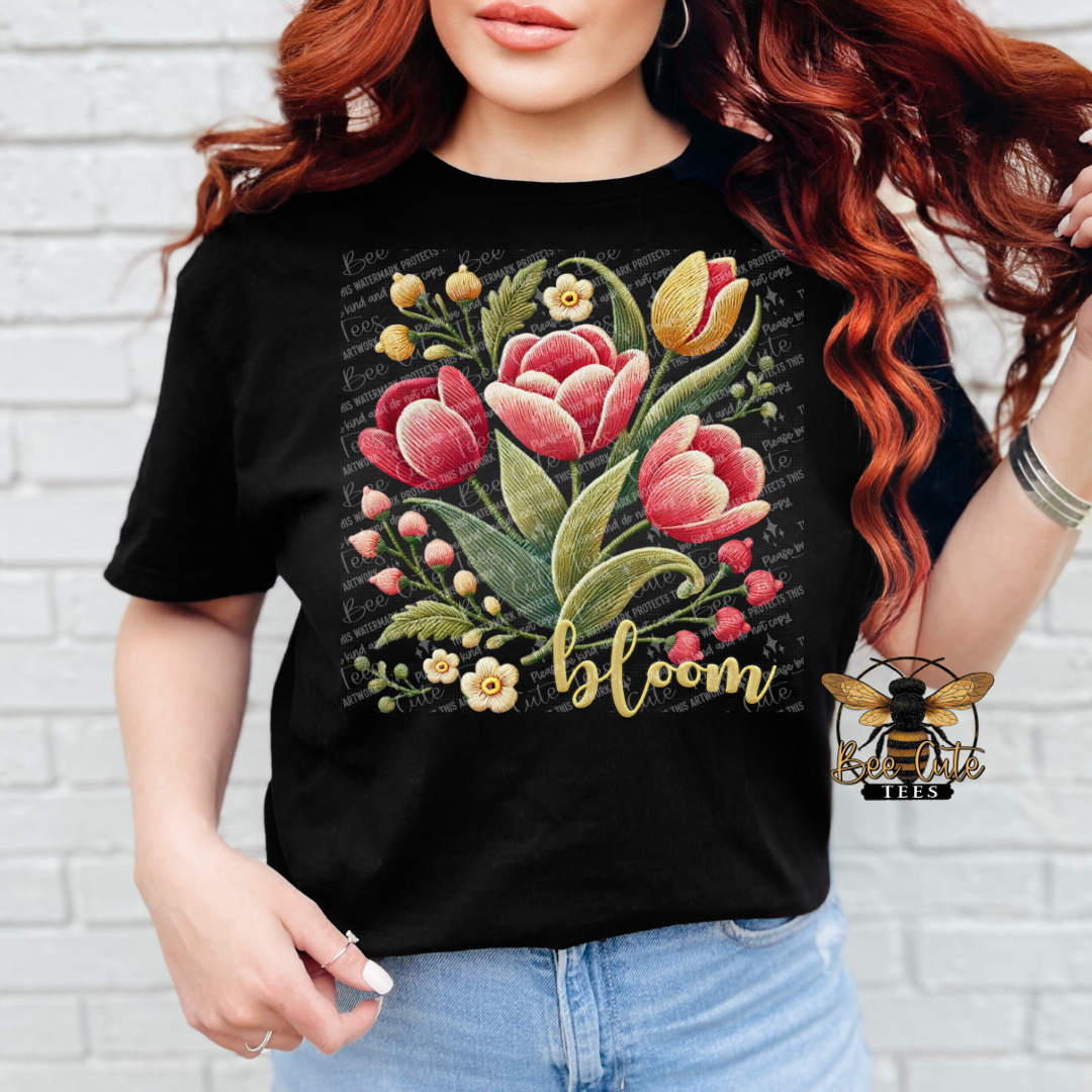 Person wearing a black t-shirt with floral design and 'bloom' text against a white brick wall.