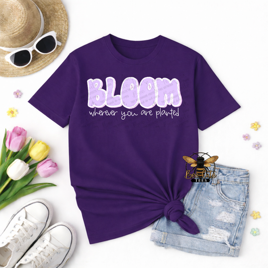 Purple t-shirt with 'Bloom wherever you are planted' text, sunglasses, tulips, and denim shorts on a white background.