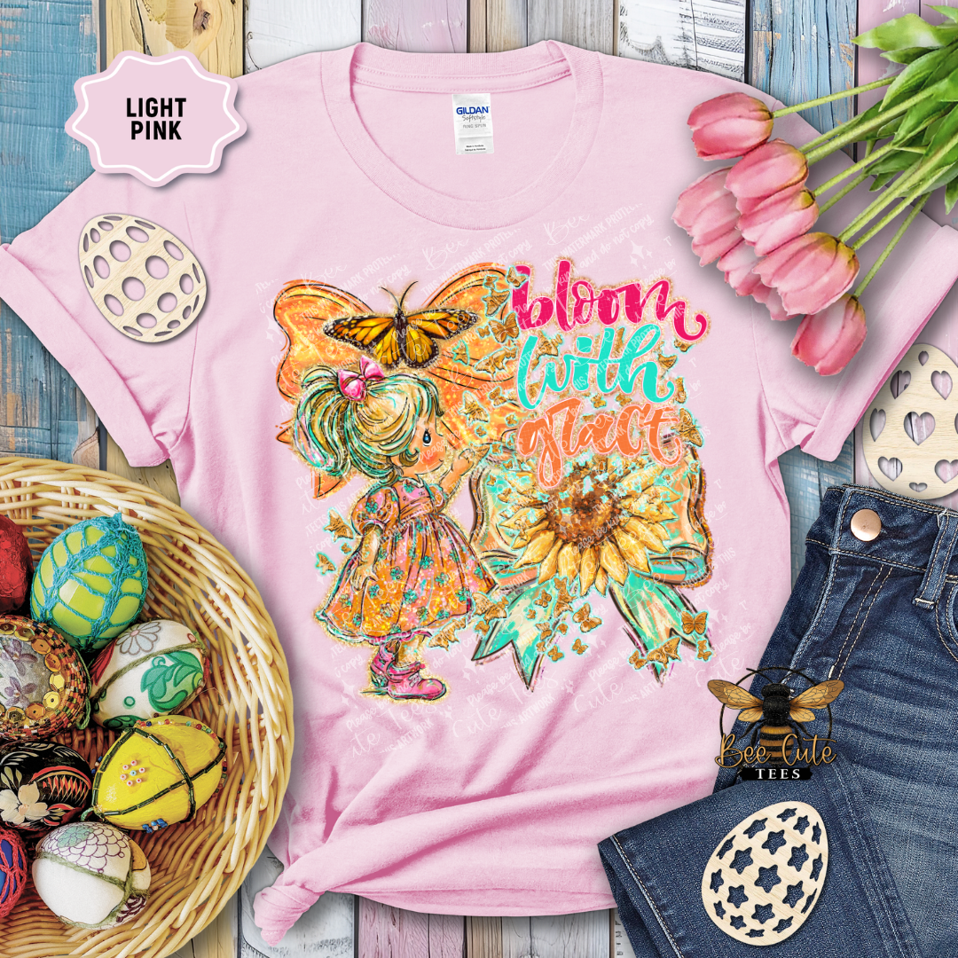 Light pink t-shirt with a colorful design of a fairy, butterfly, and sunflower, surrounded by Easter eggs and tulips.