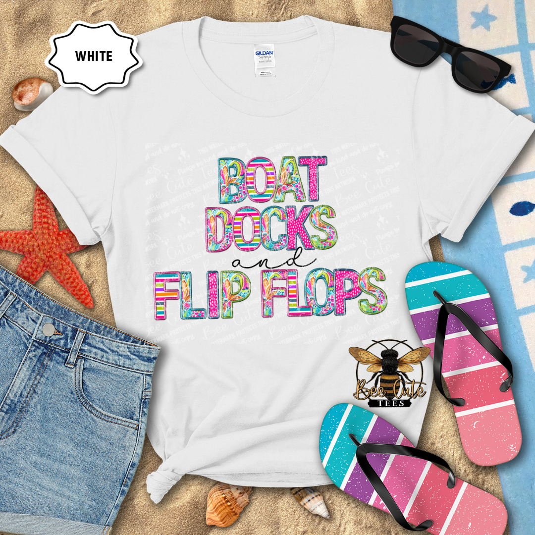 White t-shirt with colorful text 'BOAT DOCKS AND FLIP FLOPS' on a beach-themed background with sunglasses, flip flops, and denim shorts.