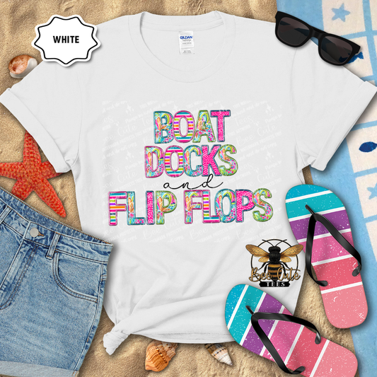 White t-shirt with colorful text 'BOAT DOCKS AND FLIP FLOPS' on a beach-themed background with sunglasses, flip flops, and denim shorts.