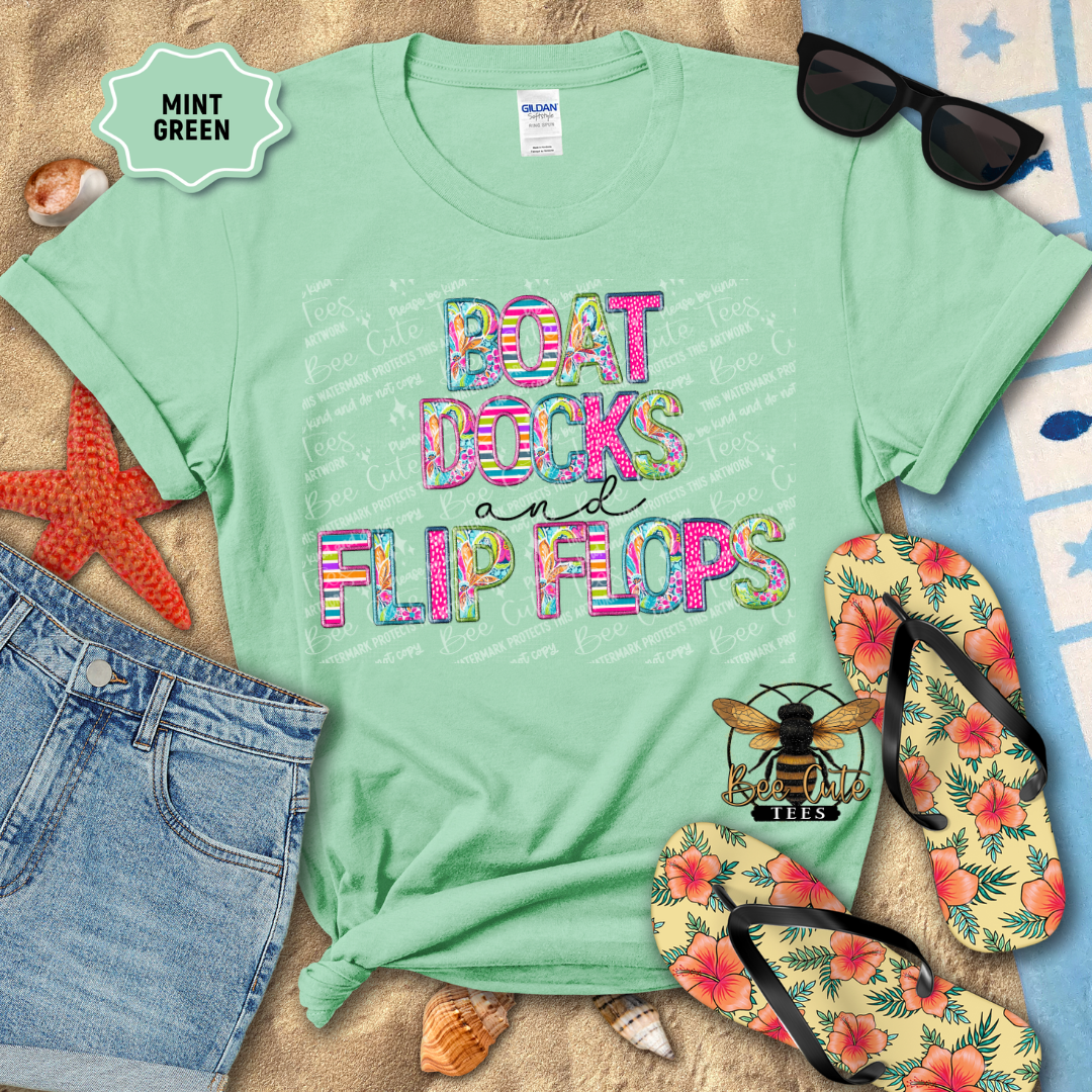 Mint green t-shirt with colorful text 'BOAT DOCKS AND FLIP FLOPS' on a beach-themed background with flip flops and sunglasses.
