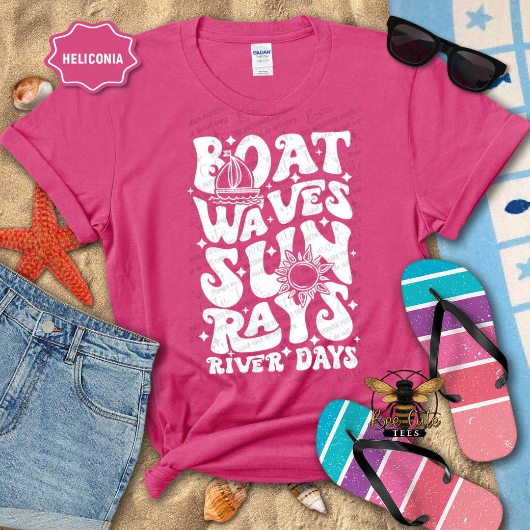 Pink t-shirt with 'Boat Waves Sun Rays River Days' design on a beach-themed background.