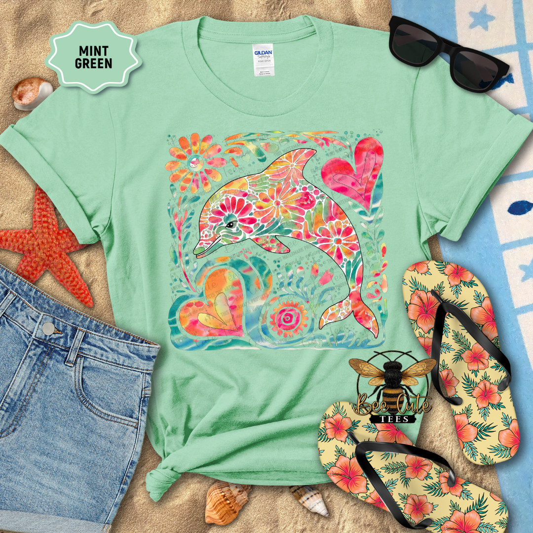 Mint green t-shirt with floral dolphin design, sunglasses, and flip-flops on a beach-themed background.