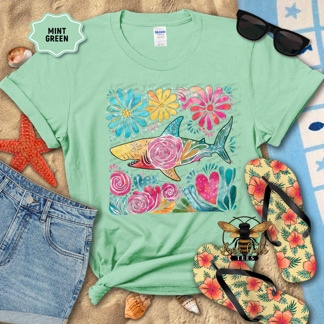 Mint green t-shirt with floral and shark design, surrounded by beach accessories.