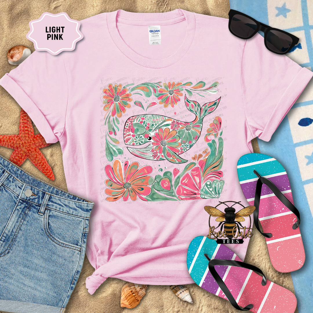 Light pink t-shirt with floral whale design, sunglasses, and flip-flops on a beach-themed background.
