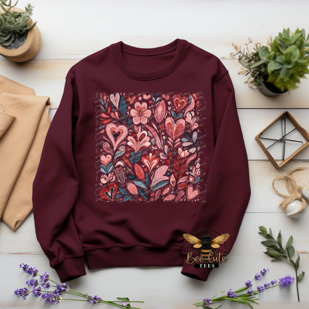 Maroon sweatshirt with floral heart design on a wooden surface with plants and fabric.
