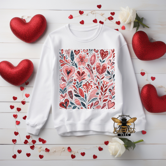 White sweatshirt with floral pattern surrounded by red hearts and flowers on a wooden surface.