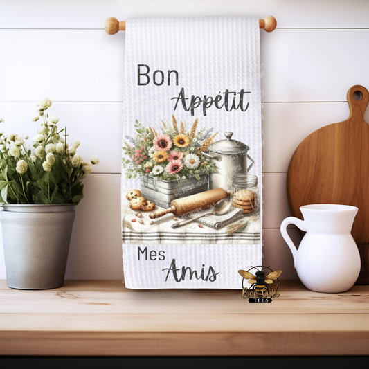 Kitchen towel with floral design and text on a wooden shelf with decor items.