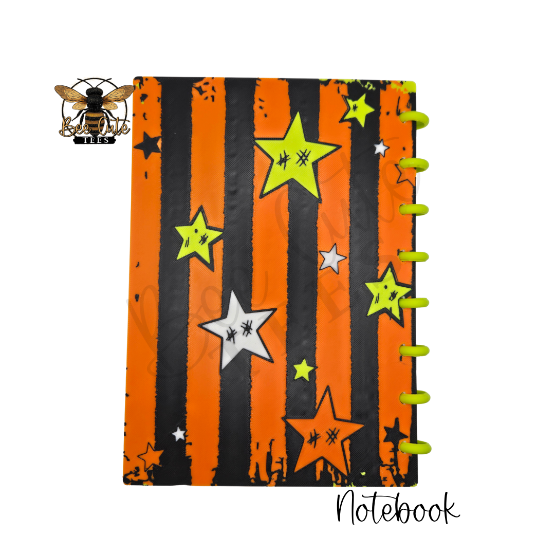 A spiral-bound notebook with a Halloween-themed cover featuring orange and black vertical stripes, lime green and white stars, and a spooky bee logo in the top-left corner. The word 'Notebook' is written in cursive at the bottom right.