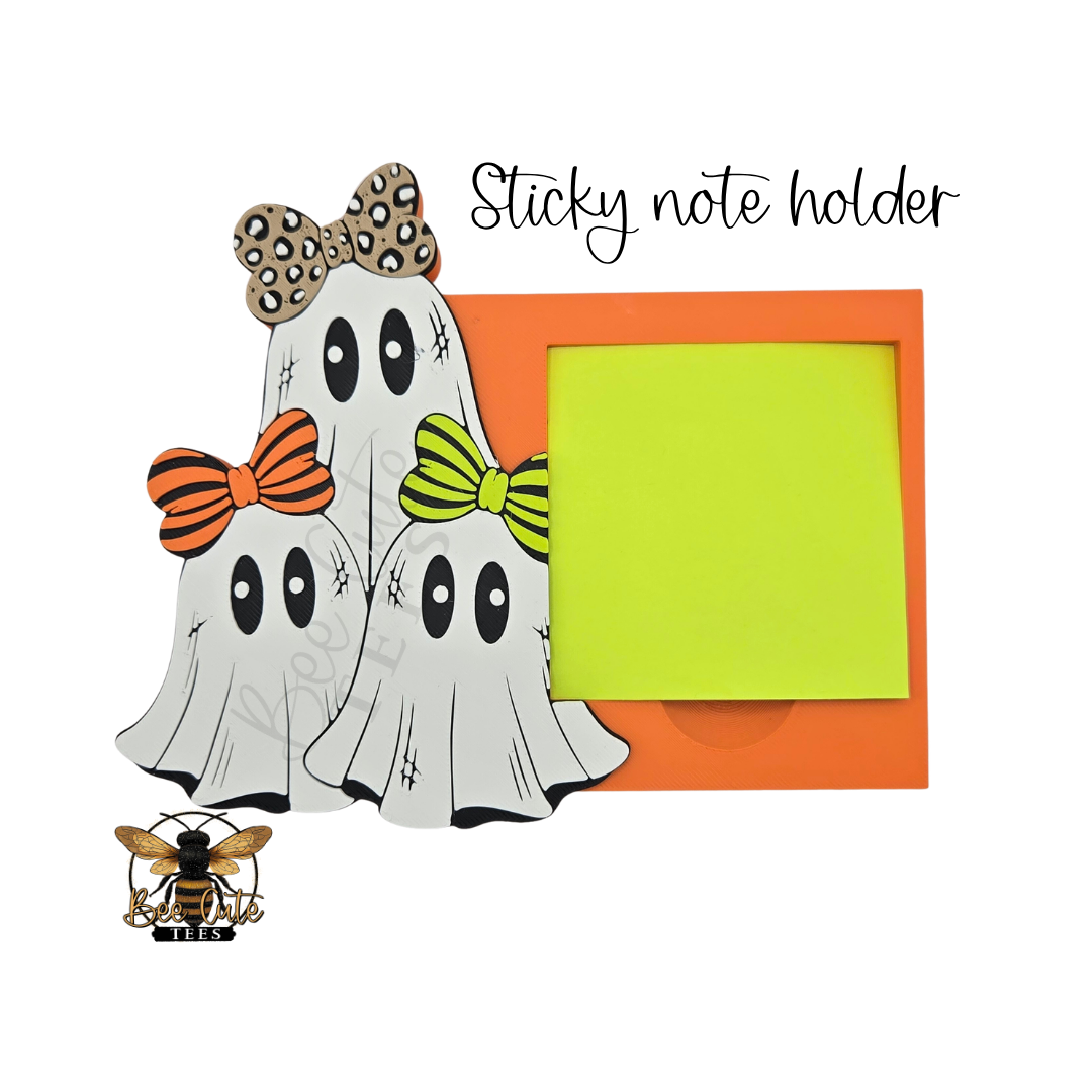 A Halloween-themed sticky note holder design featuring three cartoon ghosts with orange, brown, and green bows next to an orange square with the words 'BOO BOO' in green and orange on a black background. The text 'Sticky note holder' appears above, and a bee logo is shown at the bottom left.