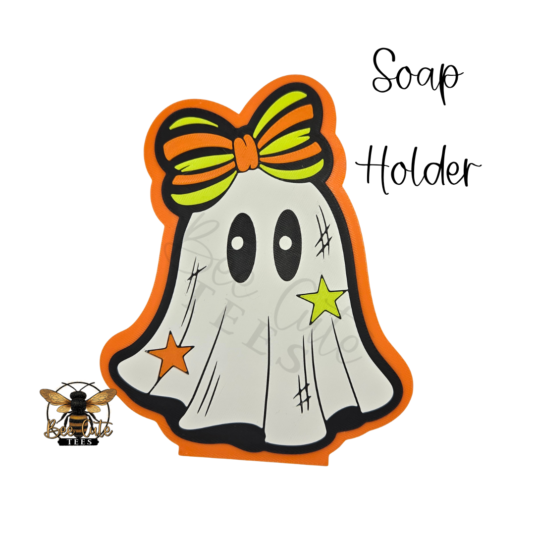A Halloween-themed ghost-shaped soap holder with an orange border, a green and orange striped bow, and star accents, shown on a white background with the words 'Soap Holder' and a small bee logo.