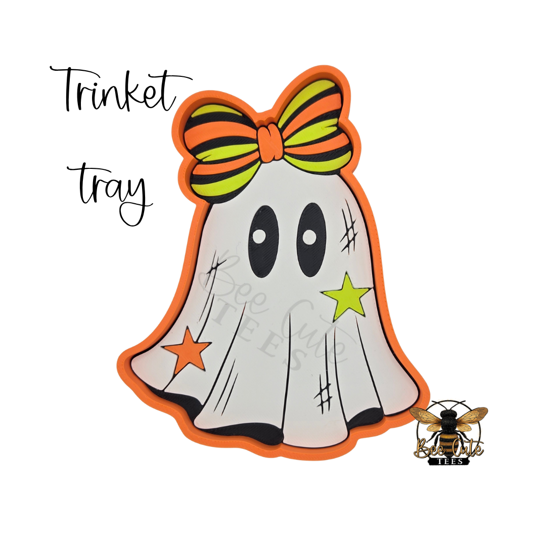 A Halloween-themed ghost-shaped trinket tray with an orange border, a striped orange and green bow, and star and scratch details, shown on a white background with the words 'Trinket tray' and a bee logo.