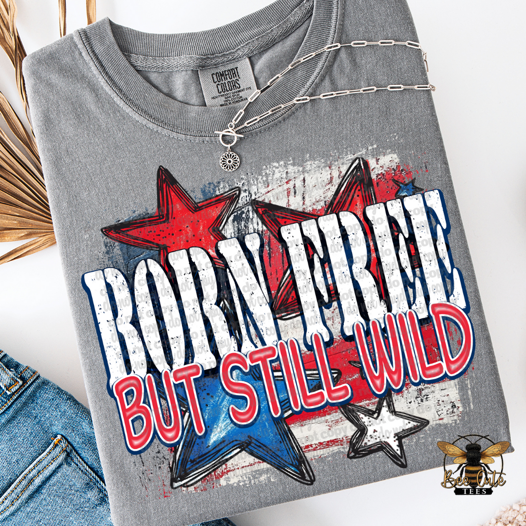 A gray short-sleeved t-shirt with a graphic print that reads ' Born Free BUT STILL WILD ' surrounded by star shapes in red, white, and blue colors.