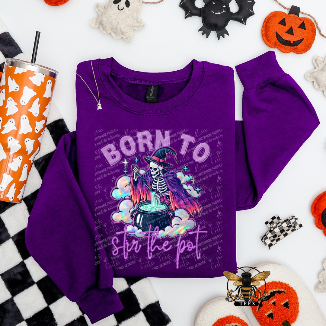 Purple sweatshirt with Halloween-themed design on a checkered tablecloth with Halloween decorations.
