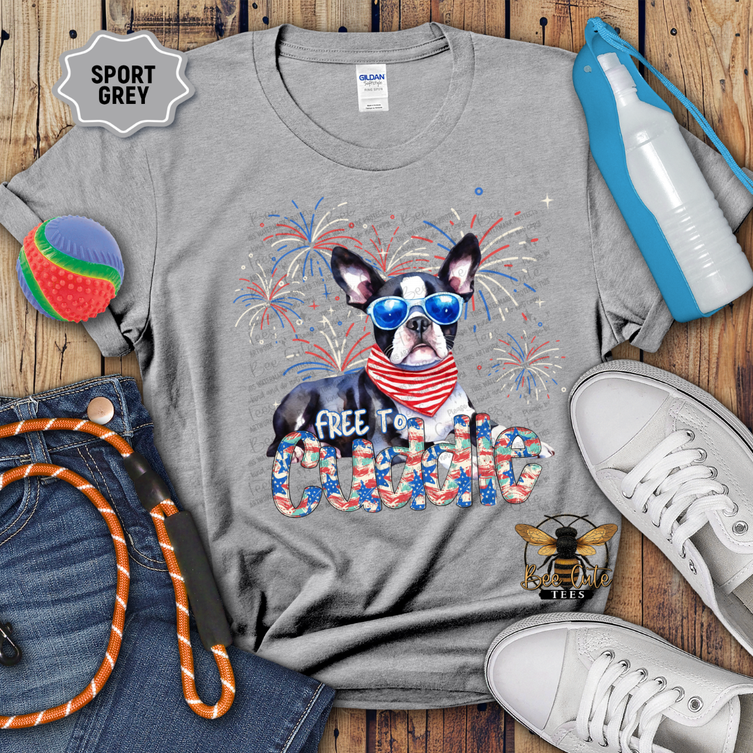 Gray t-shirt with a dog graphic and 'Free to Cuddle' text on a wooden surface with accessories.