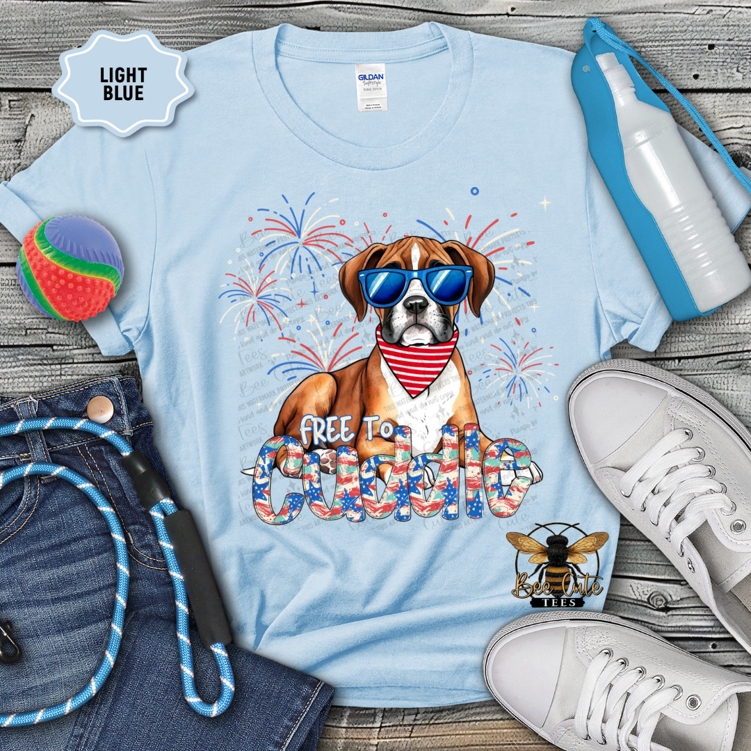Light blue t-shirt with a dog graphic and text, surrounded by jeans, shoes, and a water bottle on a wooden surface.