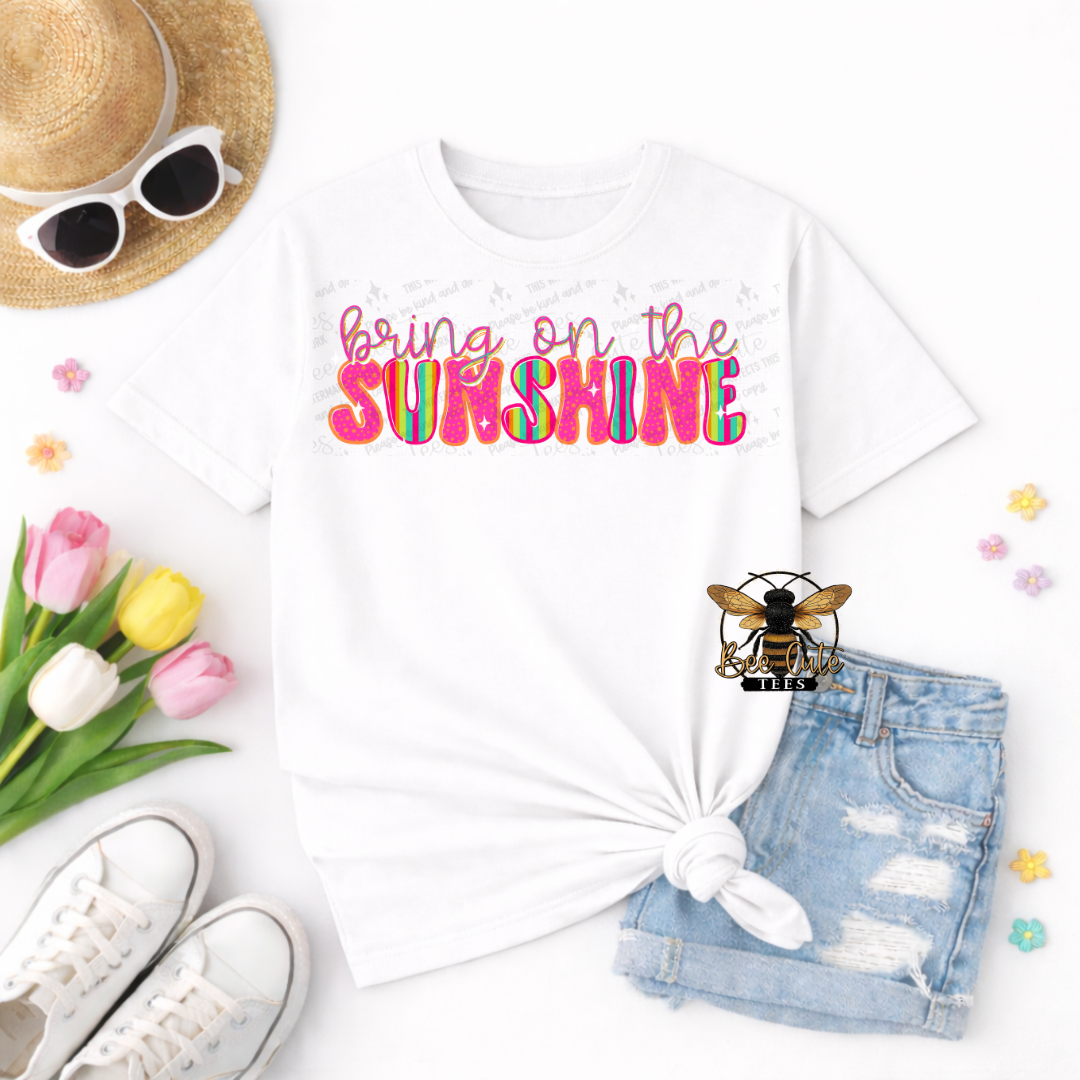 White t-shirt with 'bring on the sunshine' text, sunglasses, hat, shoes, and flowers on a white background