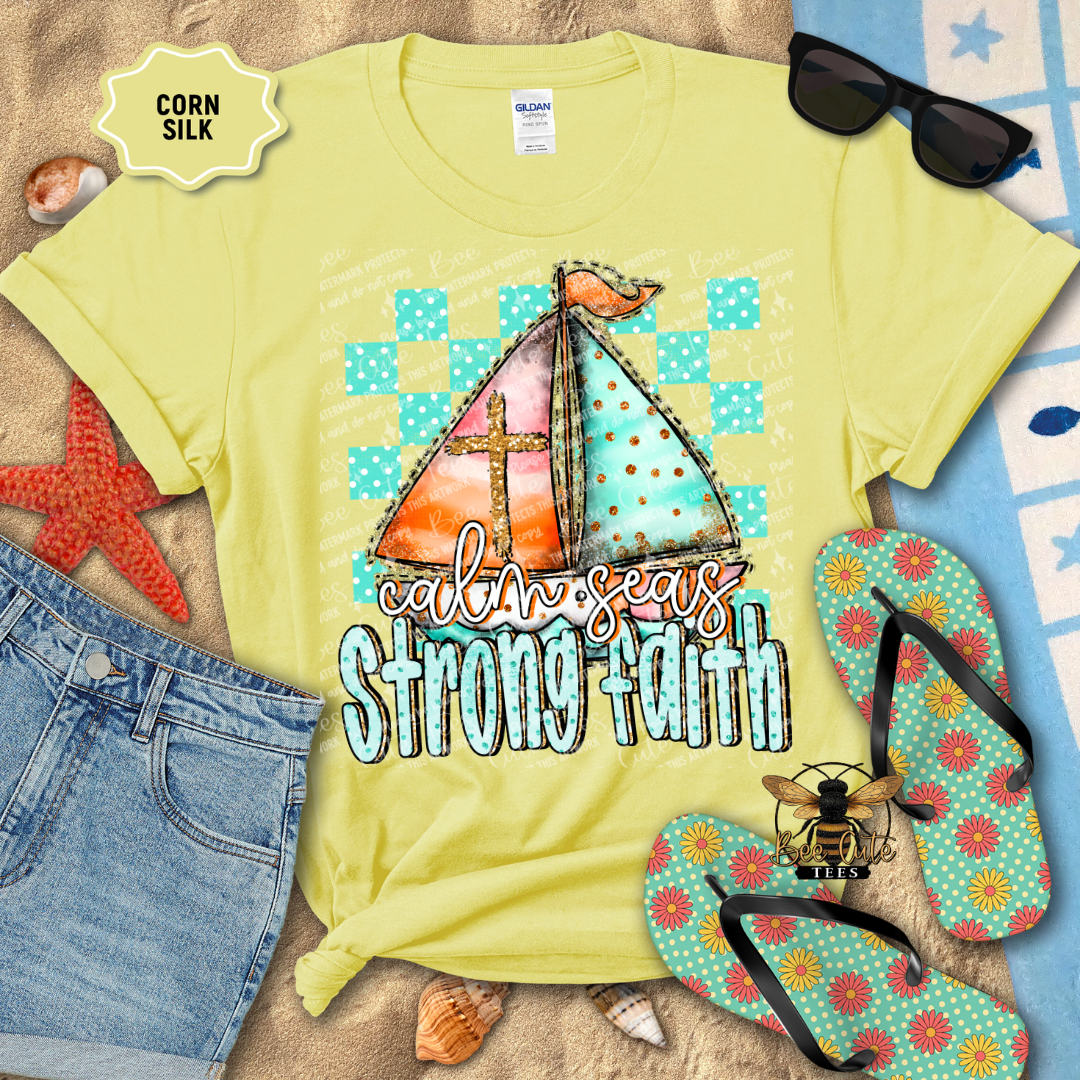 Yellow t-shirt with sailboat design and 'calm seas strong faith' text, surrounded by beach items.