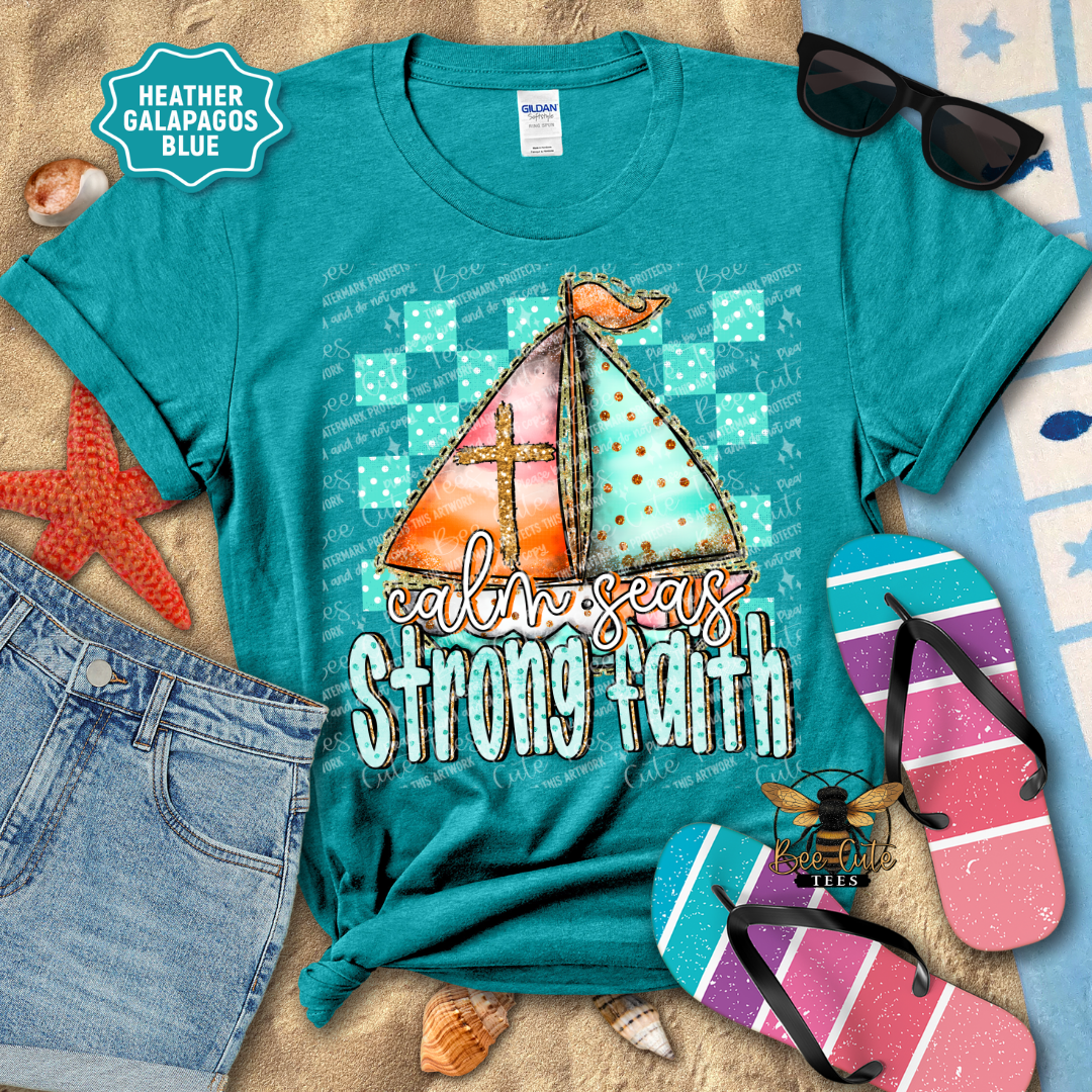 Teal t-shirt with sailboat graphic and 'calm seas strong faith' text, surrounded by beach accessories.