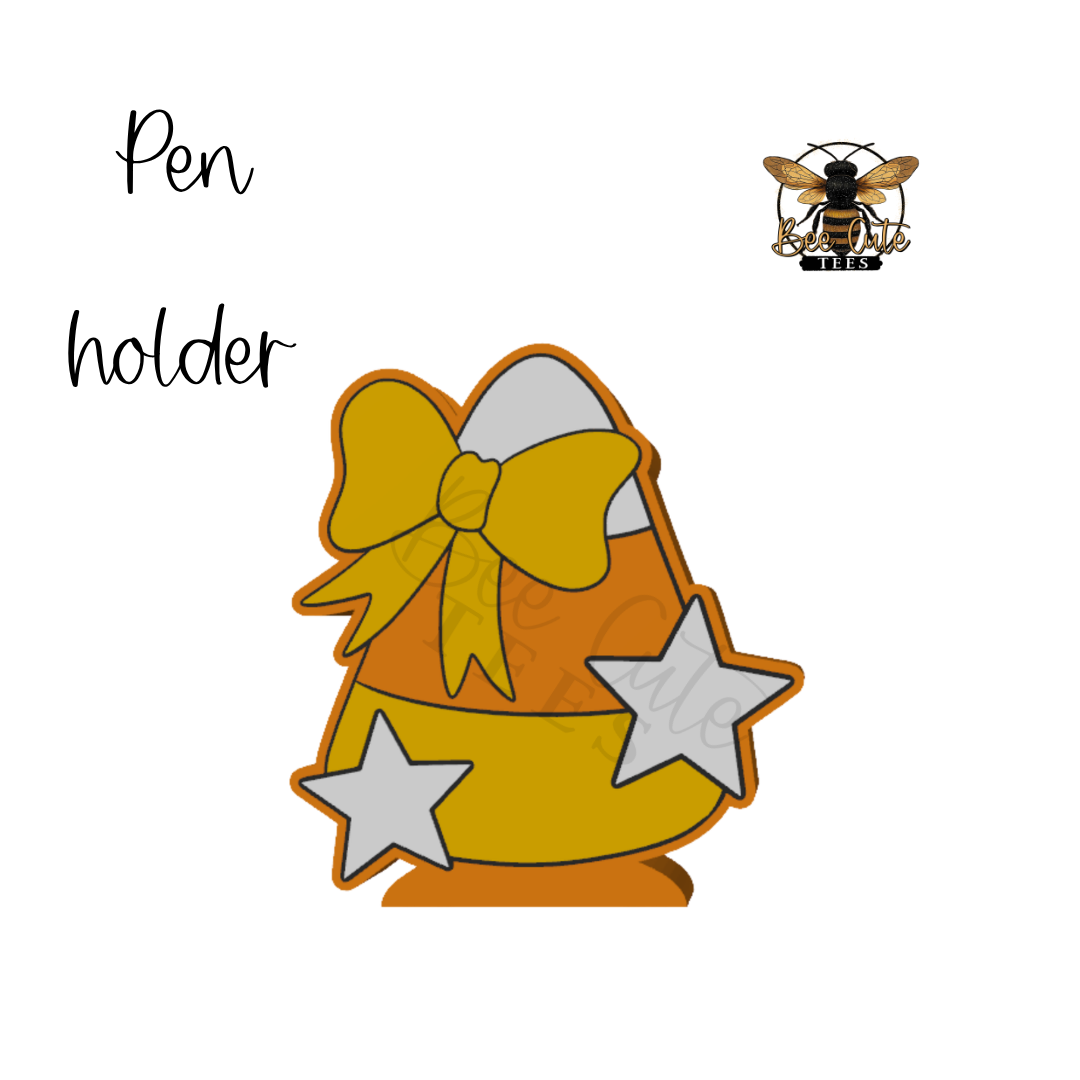 A digital graphic design of a candy corn pen holder featuring a yellow and orange candy corn body, a large yellow bow, and two white stars, with the text 'Pen holder' and a bee logo on a white background.
