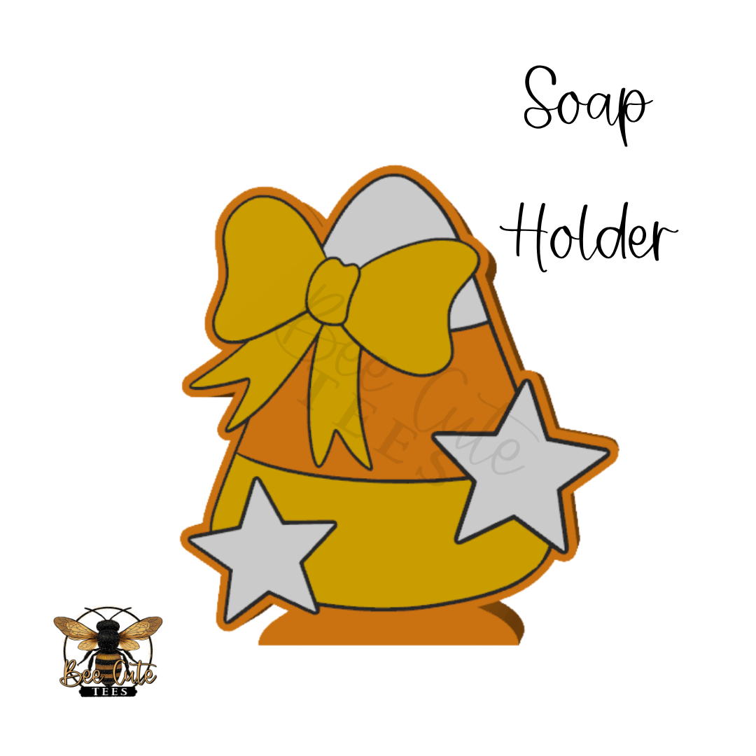 A digital graphic design of a Halloween-themed soap holder shaped like a candy corn, decorated with a yellow bow, white stars, and an orange outline, with the text 'Soap Holder' and a bee logo on a white background.