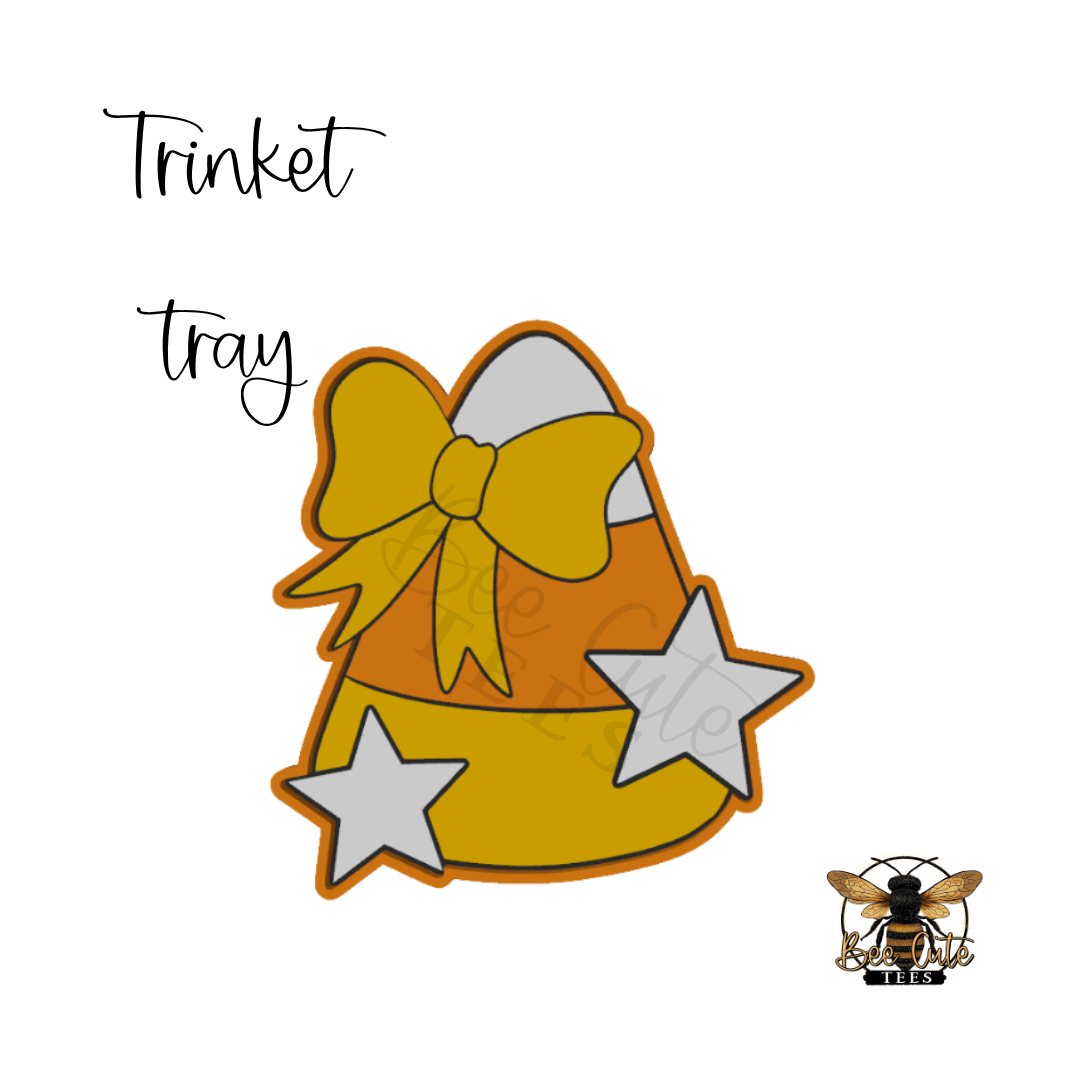 A digital graphic design of a candy corn shaped gift tray with a large yellow bow and silver stars, labeled with the text 'Trinket tray' on a white background.