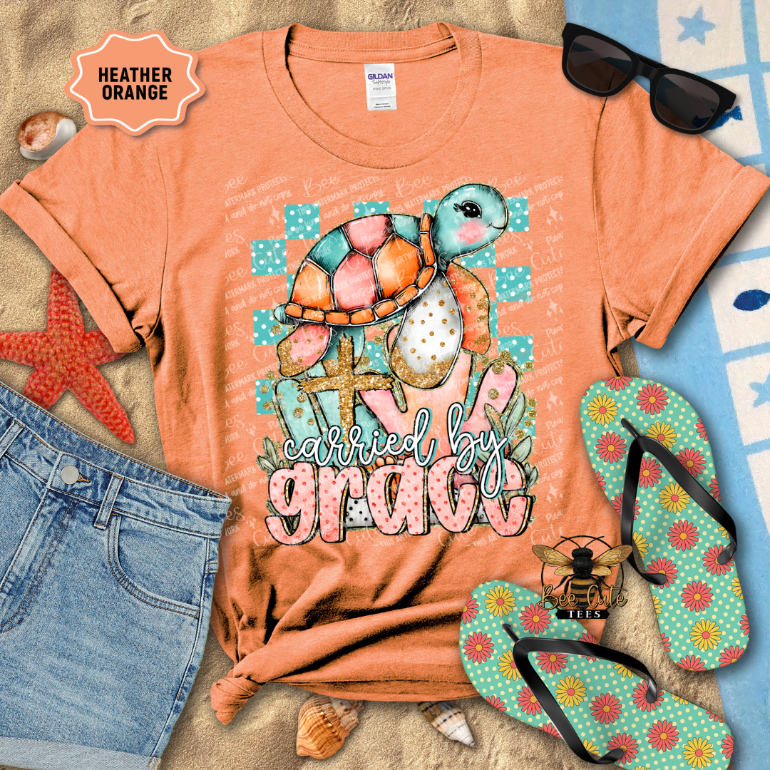 Orange t-shirt with turtle graphic and 'carried by grace' text, surrounded by beach accessories.