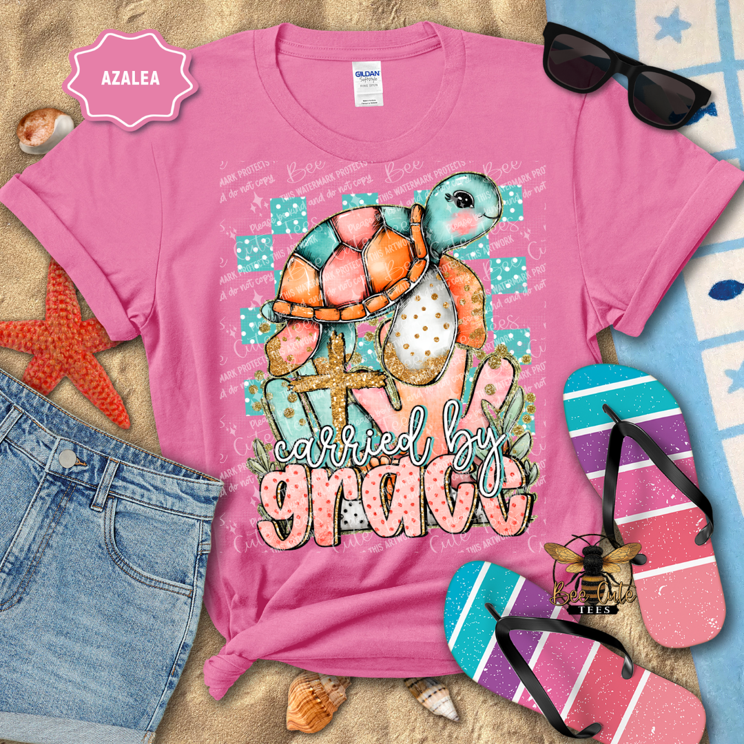 Pink t-shirt with a colorful turtle design and text, surrounded by beach accessories.