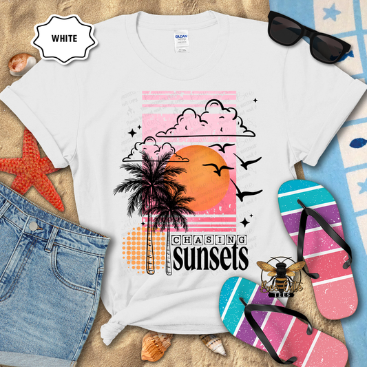 White t-shirt with 'Chasing Sunsets' design on a beach-themed background with sunglasses, flip-flops, and beach accessories.