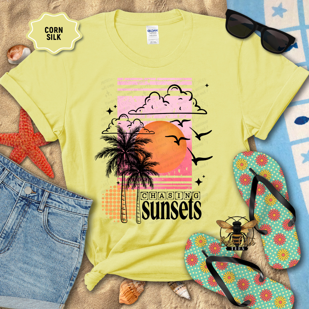 Yellow t-shirt with palm tree and sunset design, sunglasses, flip-flops, and beach accessories on a sandy background.