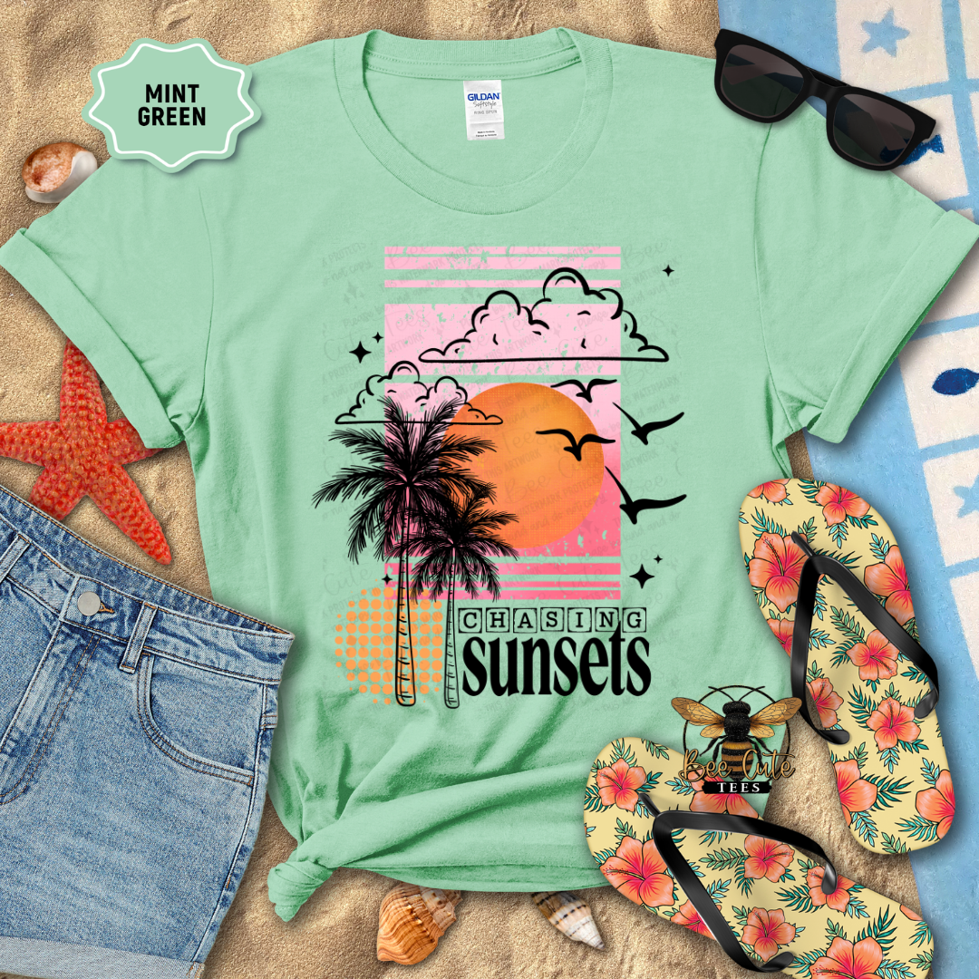 Mint green t-shirt with palm tree and sunset design, surrounded by beach accessories.