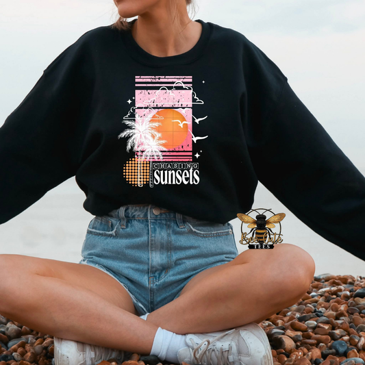 Person wearing a black sweatshirt with a sunset design sitting on pebbles.
