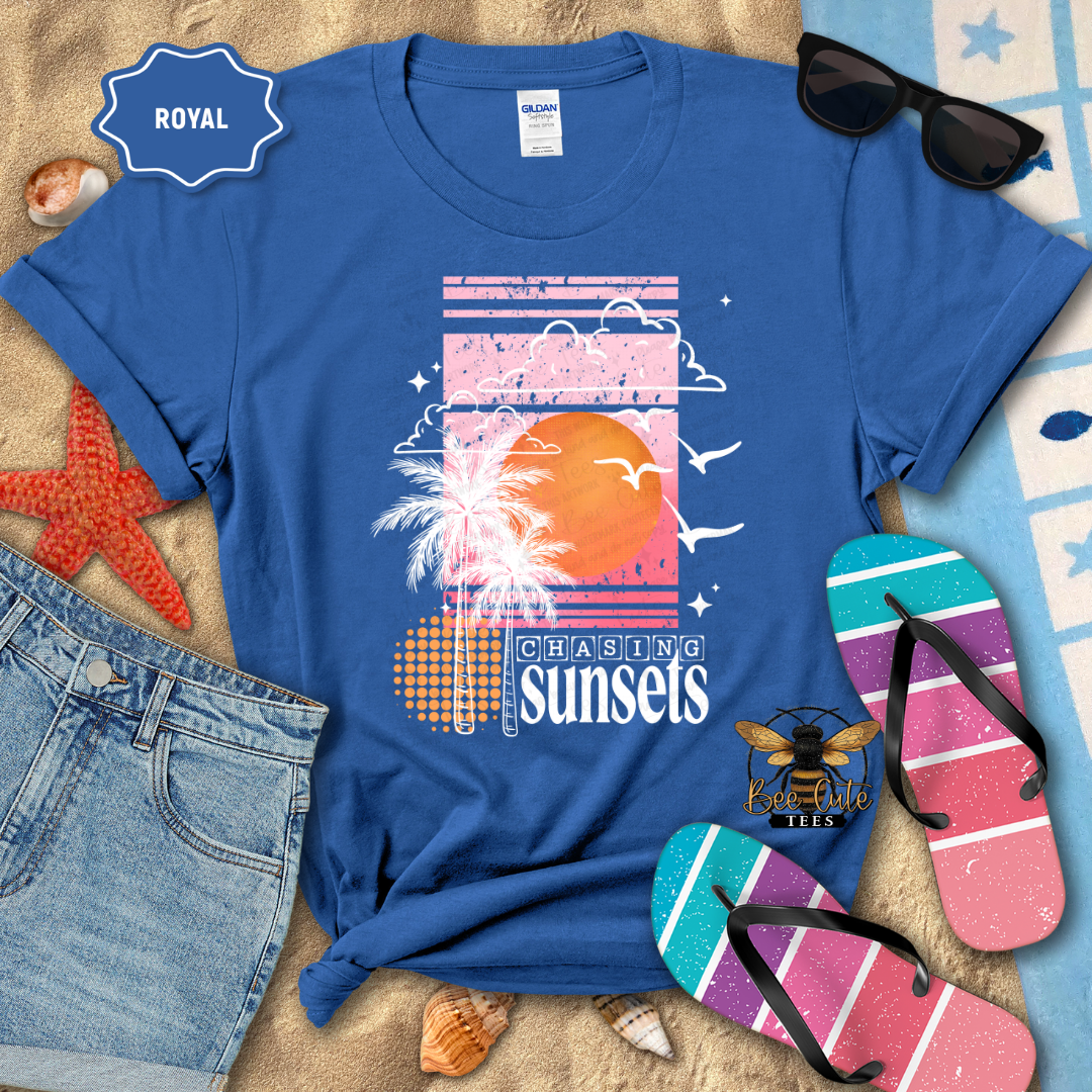 Blue t-shirt with 'Chasing Sunsets' design on a beach-themed background with sunglasses and flip-flops.